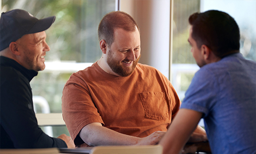 Topher praat lachend met twee collega’s aan een tafel.