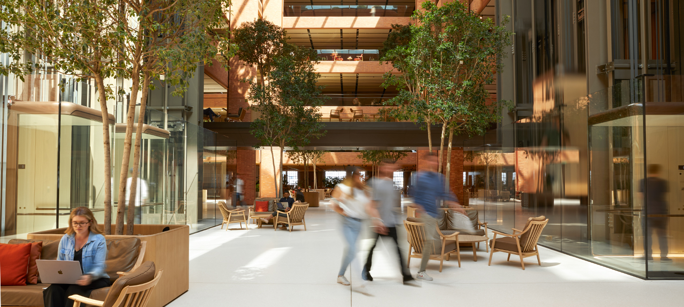 Le rez-de-chaussée de l’atrium de Battersea, baigné de lumière. On y voit plusieurs membres des équipes Apple passer, discuter et travailler en s’étant installés dans différents types de sièges.