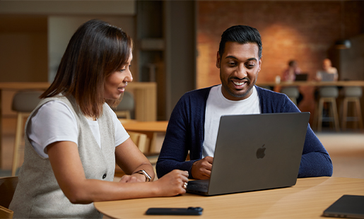 Amar, assis à une table dans un espace collectif, avec son MacBook devant lui, travaille avec une collègue.