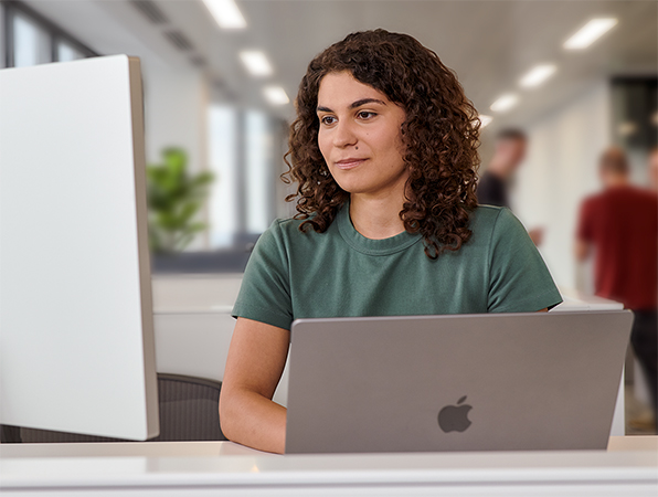 Dans un bureau, une employée Apple utilise un MacBook et un Studio Display.