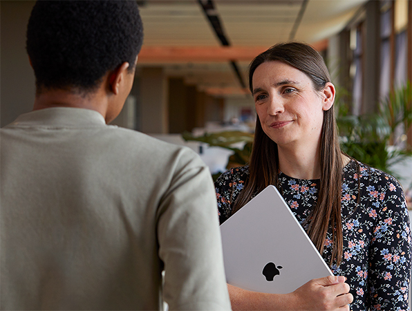 Deux collègues Apple discutent debout. La femme tient un MacBook.