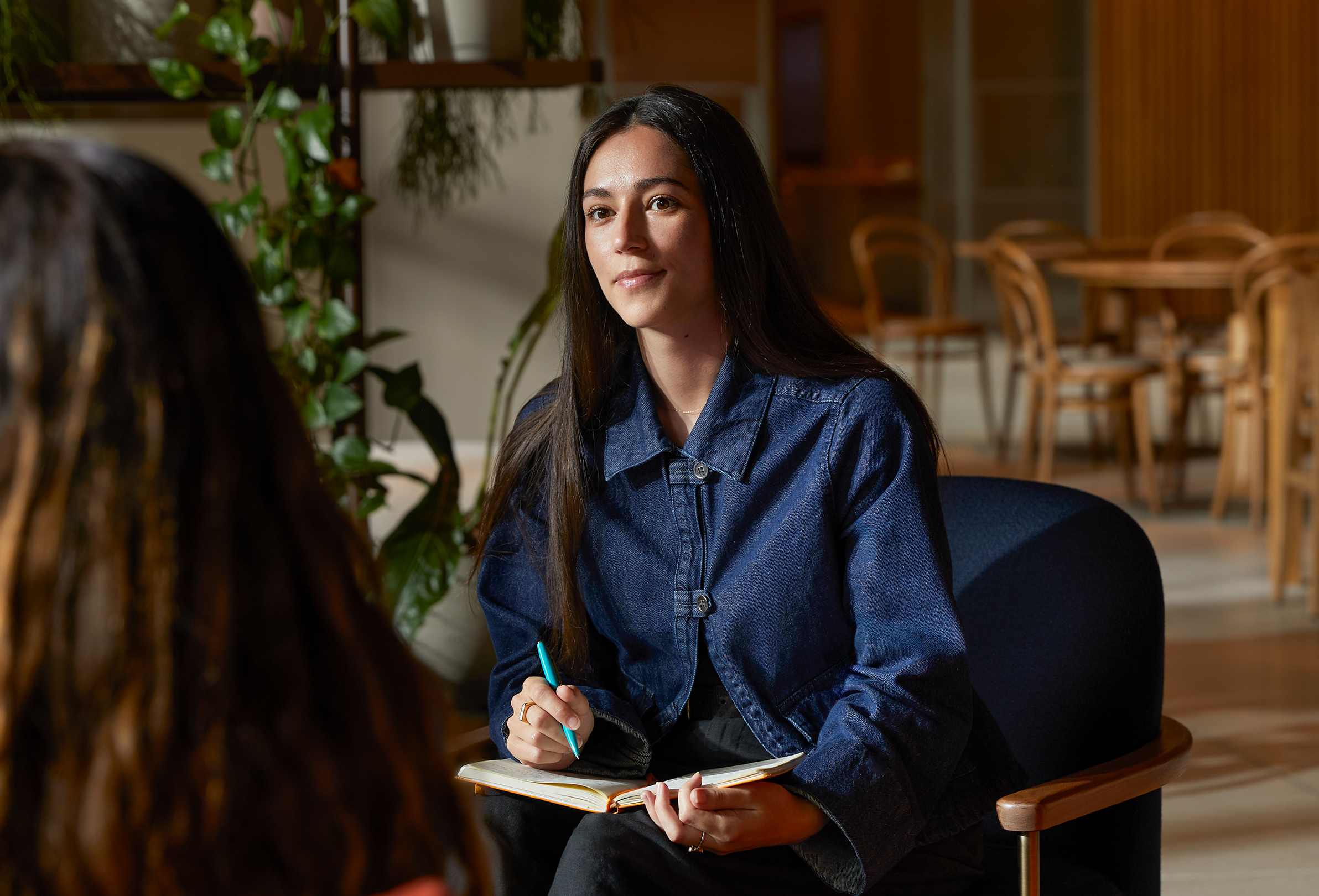 Une employée Apple est assise à une table dans un espace collectif et discute avec un autre membre de l’équipe.