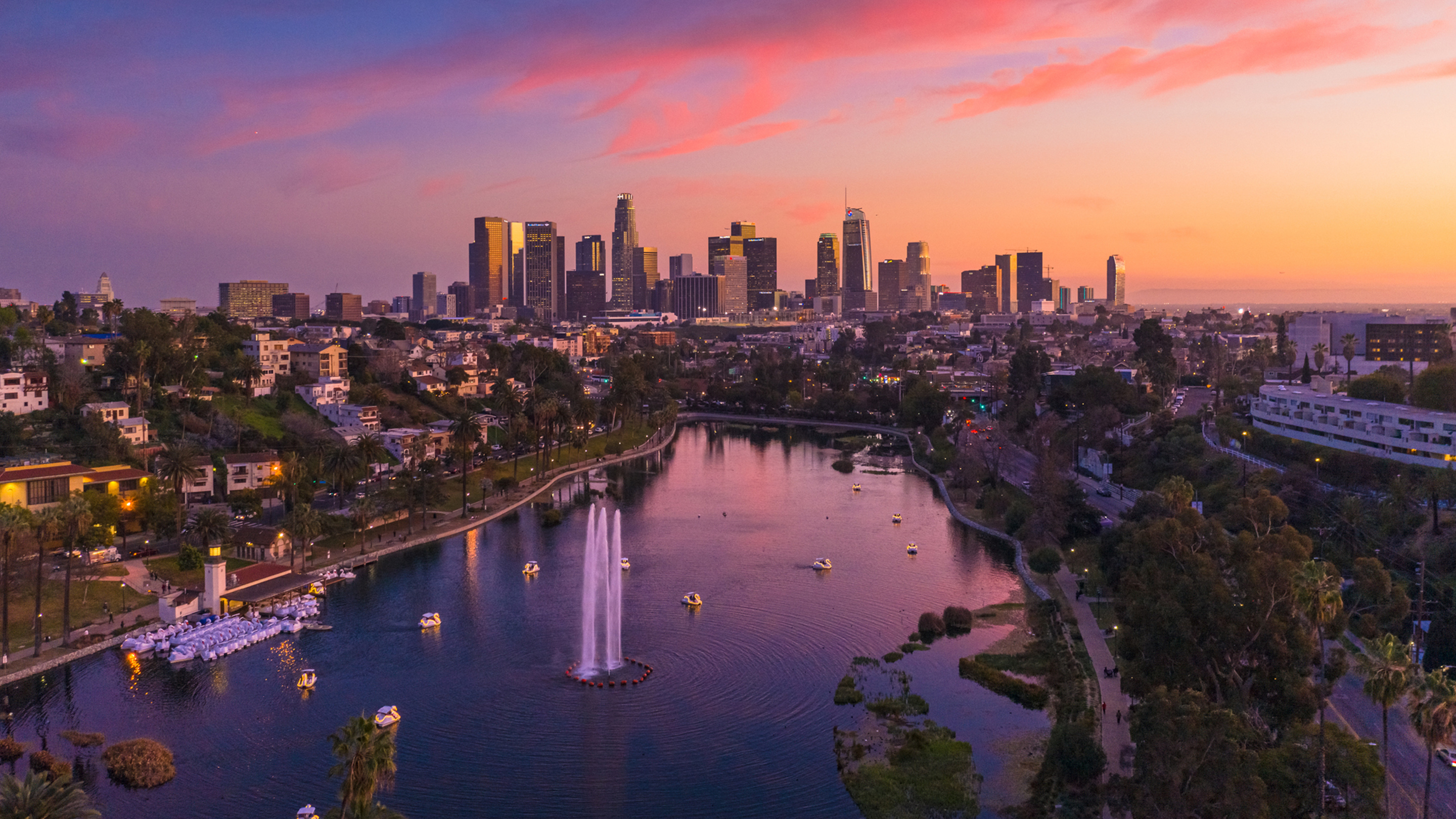 Aerial view looking toward Los Angeles skyscrapers with a park and a lake in the foreground.