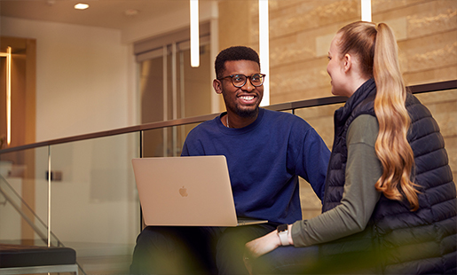 Chidi, assis avec un MacBook sur ses genoux, discute avec une collègue.