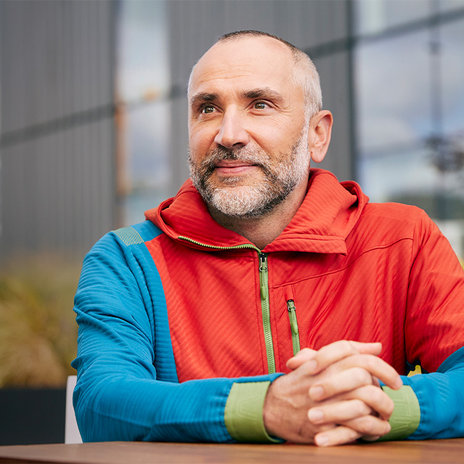 Dragos, assis dehors, sourit, le regard tourné sur le côté.