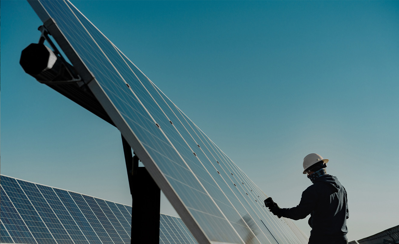 Un homme portant un casque de chantier travaille sur un grand panneau solaire en extérieur.