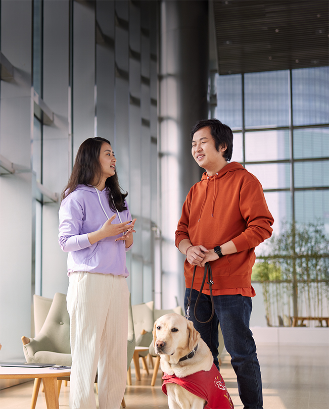 Deux employés Apple parlent dans une salle commune lumineuse, l’un tient la laisse d’un chien guide.