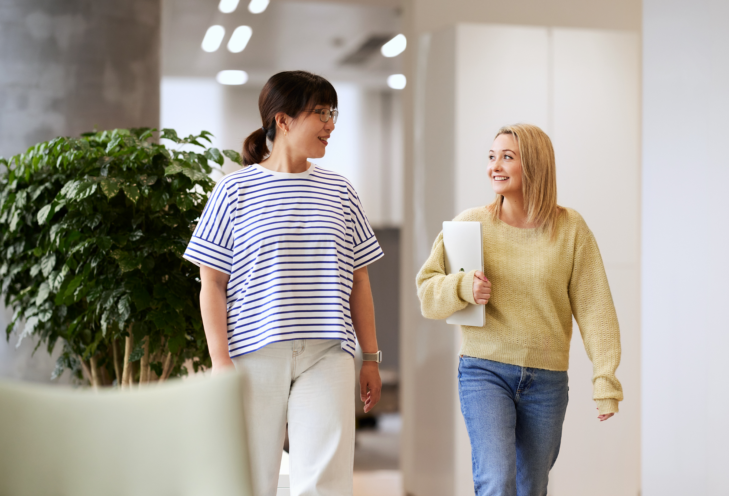 Deux employées Apple discutent en souriant et traversent un espace commun lumineux.