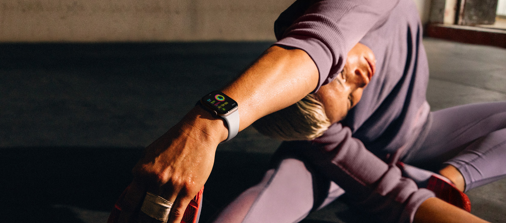 A woman on the floor stretching her arm to her leg while wearing an Apple Watch Series 10.