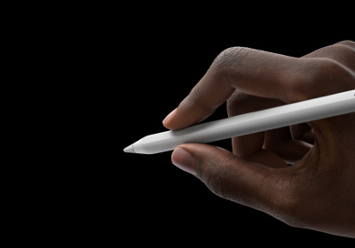 Uma mão segura o Apple Pencil Pro na posição de escrita. A ponta está voltada para a interface, que exibe uma nova paleta de ferramentas.