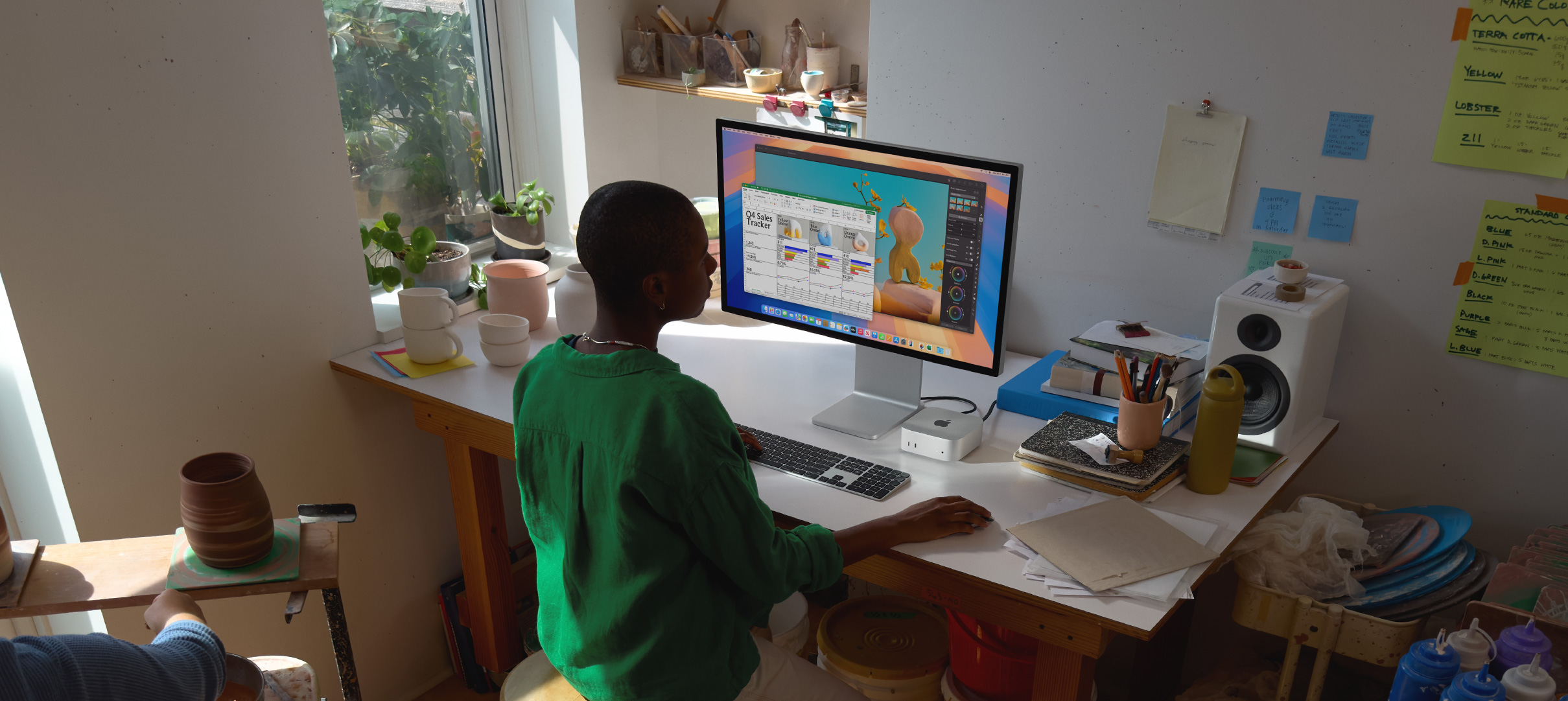 A person uses Mac mini at a desk, viewing a display screen with color app activity