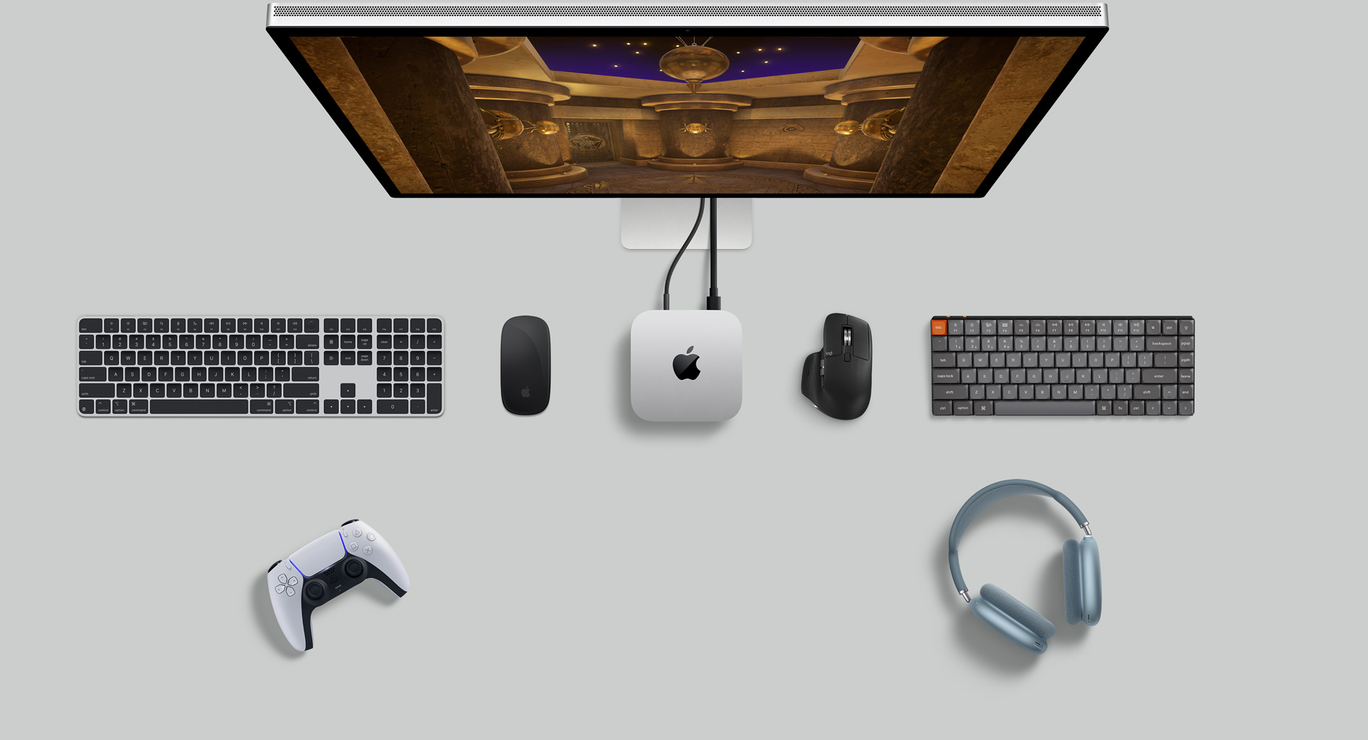 Imagem de cima do Mac mini prateado sobre uma mesa com monitor, teclados sem fio, mouse sem fio, controle para jogos e AirPods Max.