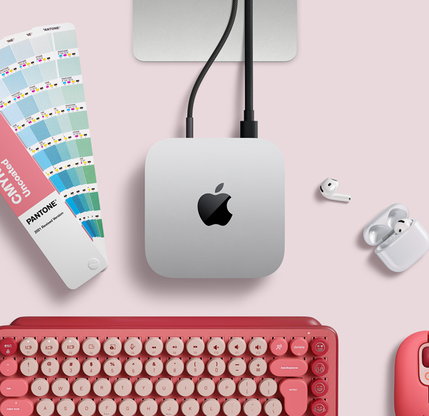 Imagem de cima do Mac mini prateado sobre uma mesa com AirPods, um teclado sem fio rosa, um mouse sem fio rosa e um catálogo de cores.